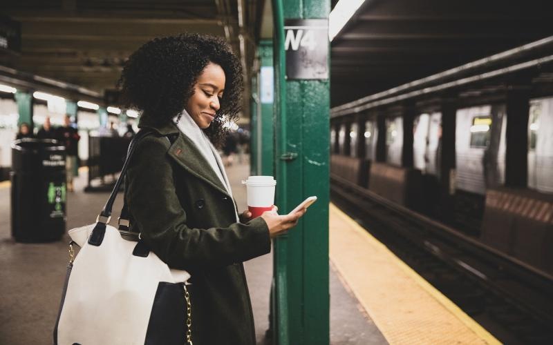 woman with a cup of coffee texts on subway station platform